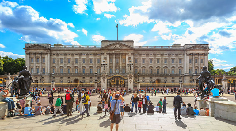 Front view of Buckingham Palace with the iconic Victoria Memorial in the foreground and blue skies above.