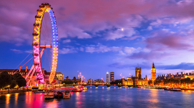 The London Eye Ferris wheel on the South Bank of the River Thames, with a clear blue sky in the background.