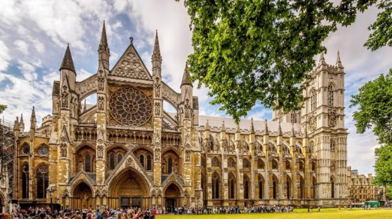 Westminster Abbey with its intricate Gothic facade, surrounded by lush greenery and a bright blue sky.